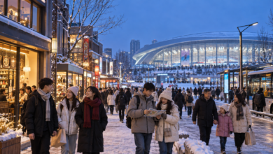 雪に包まれたスポーツ施設を背景に、来場者が周辺の商業地区で買い物や観光を楽しむ様子。